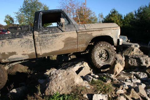 1987 Ford Bronco - Pickup truck is stuck on rocks, covered in mud. Another vehicle is visible in the background.