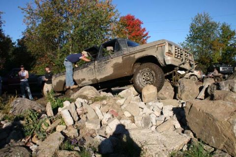 1987 Ford Bronco - A group of people watch as a muddy pickup truck navigates a rocky obstacle course.