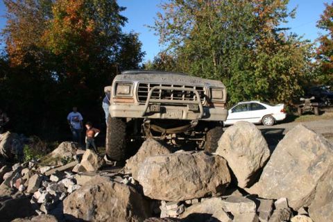 1987 Ford Bronco - This lifted 1980s Ford Bronco navigates a rocky obstacle course, with a white sedan visible in the background.