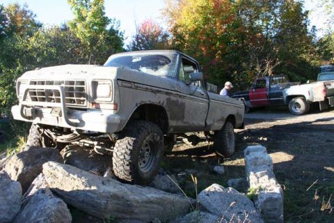 1987 Ford Bronco - Mud-covered 1979 Ford F-Series pickup truck is shown off-road on a rocky terrain with another truck in the background.