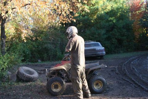 1987 Ford Bronco - A muddy sedan is parked off-road next to an ATV, suggesting off-road activity.