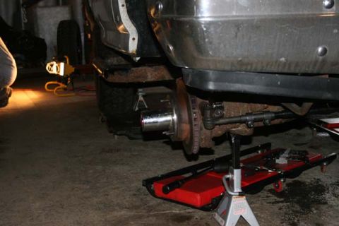 1987 Ford Bronco - Undercarriage of a vehicle, likely from the 1980s, undergoing maintenance with visible rust and repair equipment.