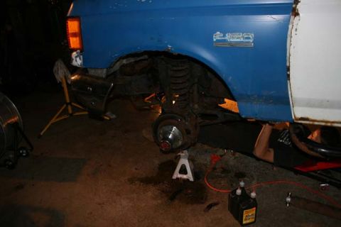 1987 Ford Bronco - A blue and white truck is shown from the side with its front wheel removed and supported by a jack stand, indicating ongoing maintenance or…