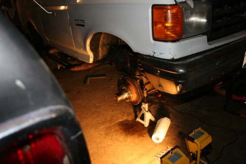 1987 Ford Bronco - The front wheel assembly of a truck is exposed while it's supported by jack stands, with another vehicle partially visible.