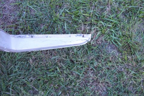 1988 Ford E250 - A silver bumper section lies on the grass, showing signs of wear.
