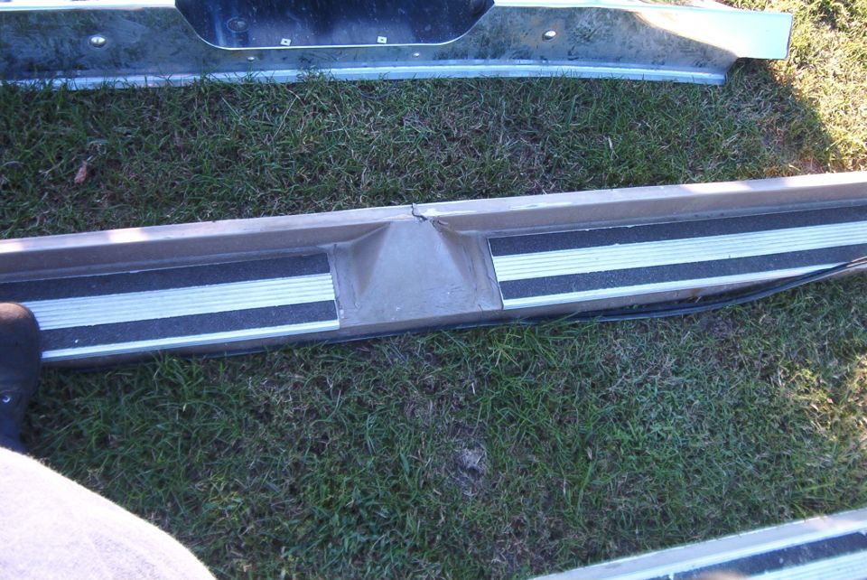 Close-up of a metal step bumper with black and silver non-slip strips. A crack is visible in the center