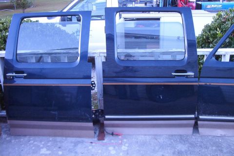 1988 Ford E250 - Multiple vehicle doors are displayed outdoors, leaning against a railing.