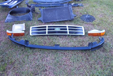 1988 Ford E250 - Various vehicle parts, including a Ford grille and radiator, are displayed on a grassy surface.