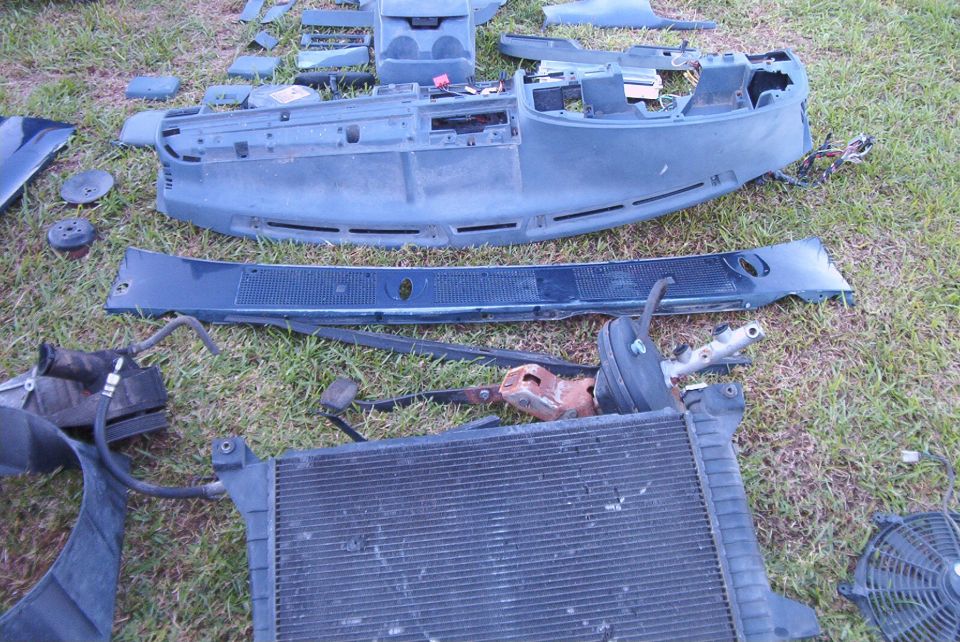 Disassembled blue dashboard, radiator, and fan laid out on grass