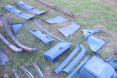 1988 Ford E250 - Various automotive parts, including interior panels and leaf springs, are displayed on a grassy surface.