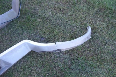 1988 Ford E250 - A damaged bumper part lies on the grass, indicating it is no longer attached to a vehicle.