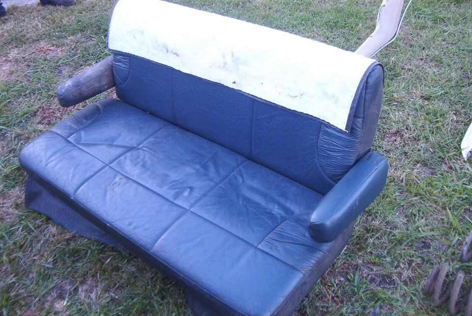Dark blue leather van bench seat with torn seatback exposing white foam, sitting on grass