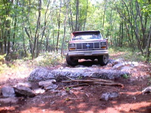 2001 Ford Escape - A red 1980s Ford pickup truck navigates a challenging rocky path through a dense forest.