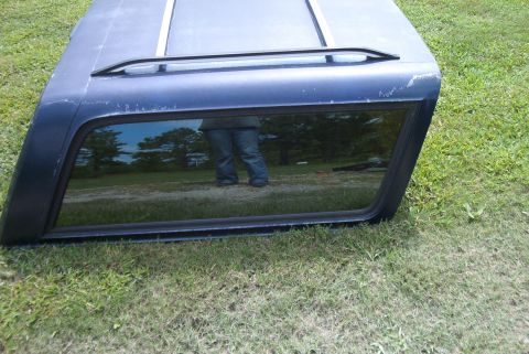1988 Ford E250 - A dark blue truck cap with a tinted window and roof rack is shown resting on a grassy surface.