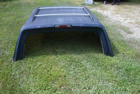 1988 Ford E250 - A dark blue truck cap with roof rack rails is shown from the rear, sitting on a grassy area.