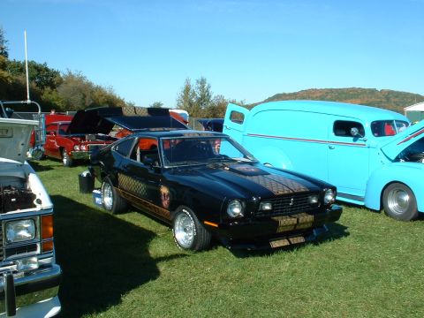 1978 Ford Mustang II - A black 1978 Ford Mustang II is parked on a grassy field with other vehicles, including a blue panel van.