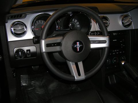 2007 Ford Mustang - The interior of a car shows a steering wheel with a Mustang emblem and a dark dashboard.