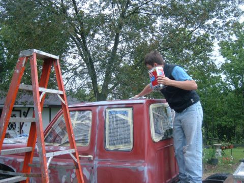 1985 Ford F-150 - A person is preparing a red truck cab for paint, using sandpaper and a can of product.