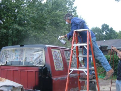 1985 Ford F-150 - A person spray paints the cab of a red and black truck while standing on an orange ladder.