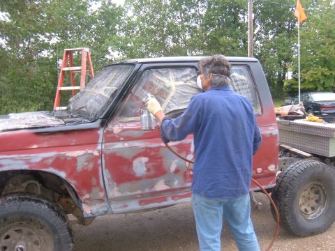 1985 Ford F-150 - A person is spray painting a truck that is undergoing body work and preparation for a new paint job.