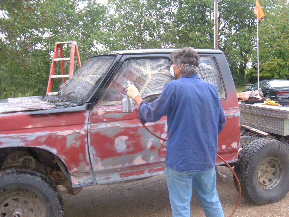 guy spray painting a red truck body that's prepped for paint