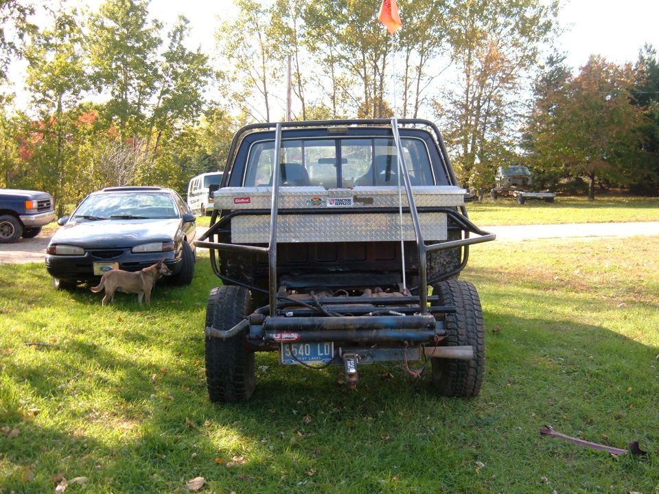 Rear view of lifted black Ford pickup with tube bed, diamond-plate toolbox and winch on grass