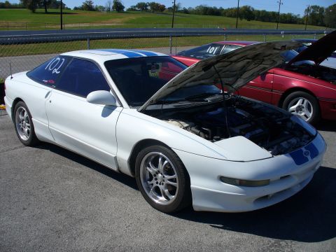 1991 Ford Probe - A white 1991 Ford Probe with blue racing stripes is parked with its hood open, alongside another car.
