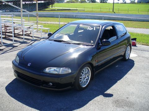 1991 Ford Probe - Black hatchback with racing numbers on windshield parked at a track. The vehicle is not a 1991 Ford Probe.