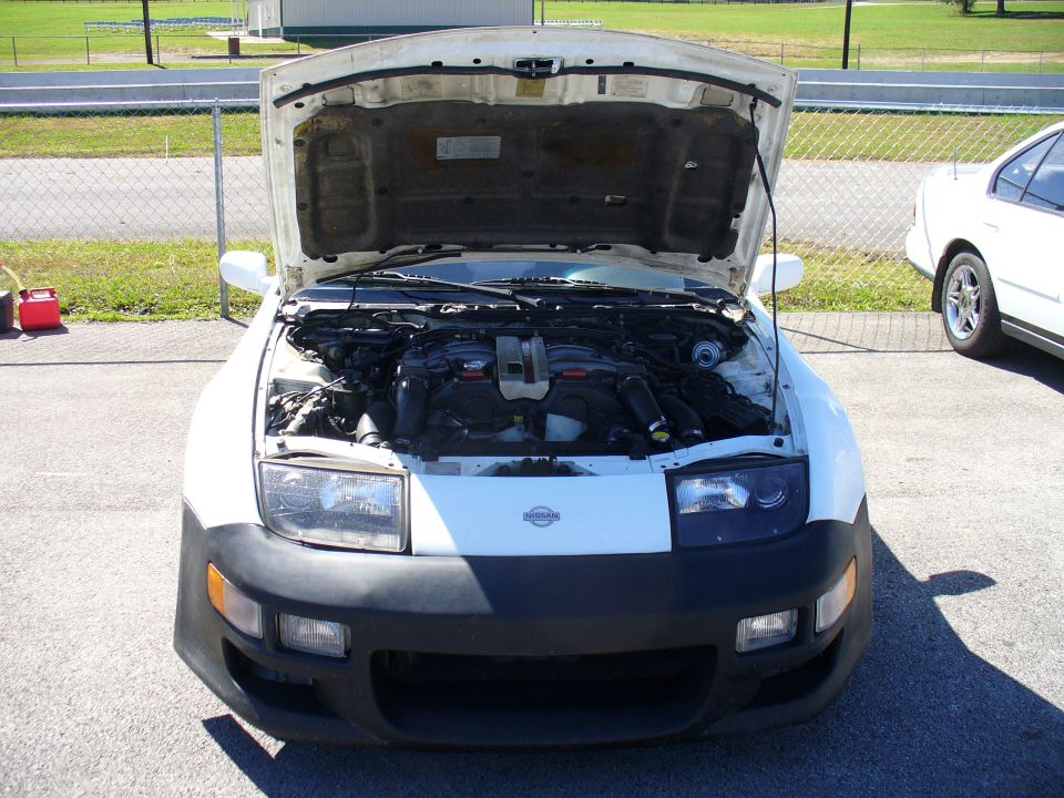 White Nissan 300ZX with hood open, showing engine bay. Another white car is parked to the right