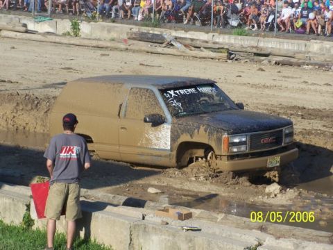 2005 Ford Excursion - A GMC SUV is stuck in the mud during a competition, with a crowd watching from the sidelines.
