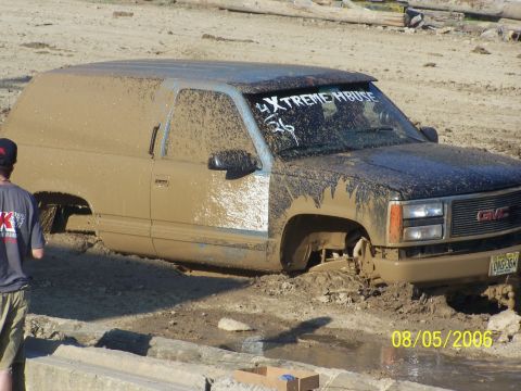 2005 Ford Excursion - A GMC Suburban is stuck deep in mud, with a person standing nearby observing the scene.