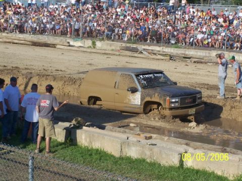 2005 Ford Excursion - A GMC SUV navigates a muddy obstacle course, with a large crowd observing the event.