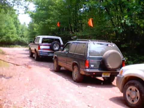 2001 Ford Escape - Several off-road vehicles are parked on a dirt path surrounded by trees, with orange flags visible in the background.