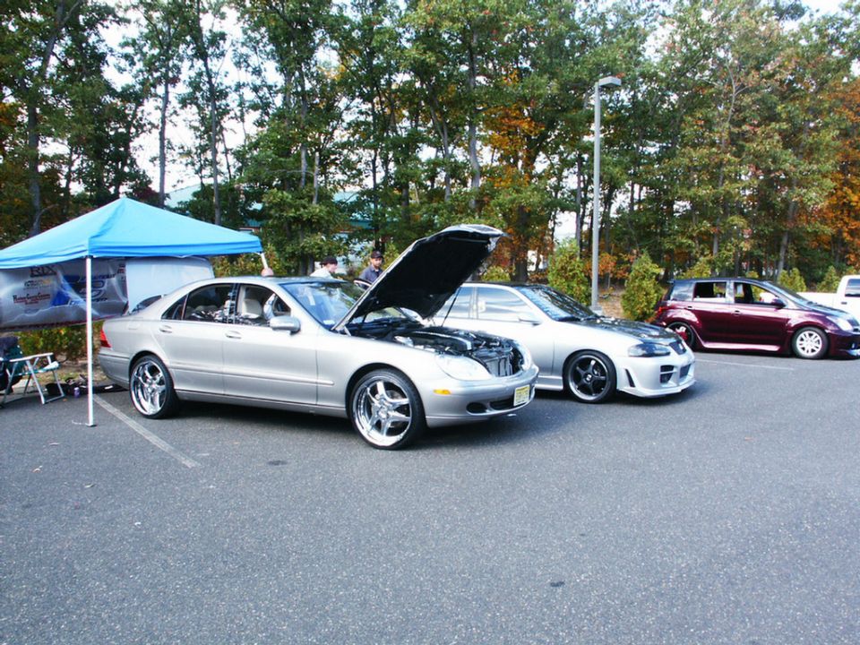 Silver sedan with hood open, custom wheels, parked at an outdoor event