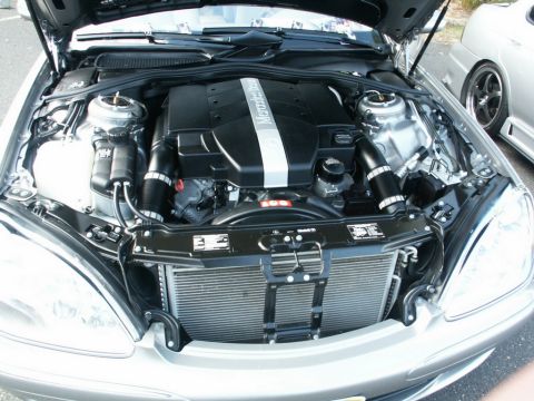 2001 Mercury Grand Marquis - The engine bay of a silver Mercedes-Benz is shown, with the engine cover prominently displaying the brand's name. A second vehicle is parti…