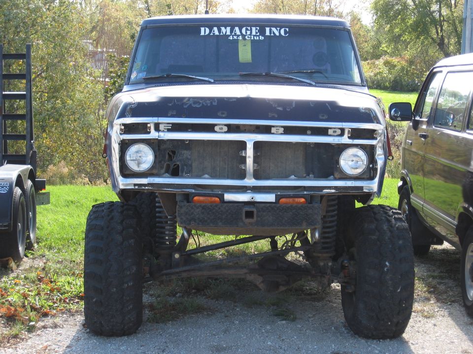 Black 1977 Ford F-150 with lifted suspension and large tires, front view. "DAMAGE INC 4x4 Club" sticker on windshield