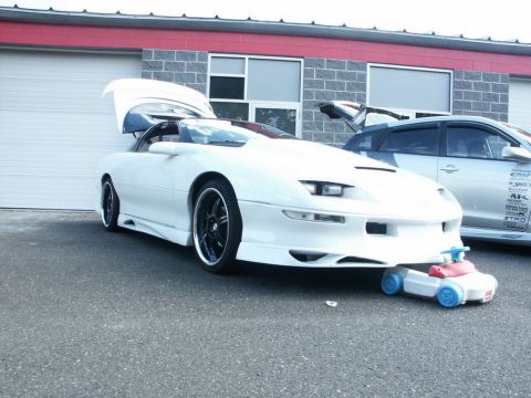 2001 Mercury Grand Marquis - A white sports car with its doors open is parked next to another vehicle, with a toy car positioned beneath its front bumper.