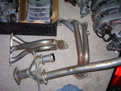 1993 Mazda MX-6 - Various car exhaust components, including manifolds and pipes, are displayed on a carpeted floor.