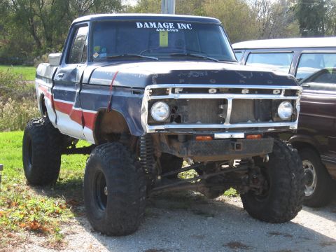1977 Ford F-150 - This modified Ford pickup features oversized tires and a lifted suspension, with a distinctive red, white, and blue stripe on the fender.