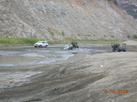 1985 Ford Bronco - Several off-road vehicles navigate a challenging muddy terrain near a quarry.