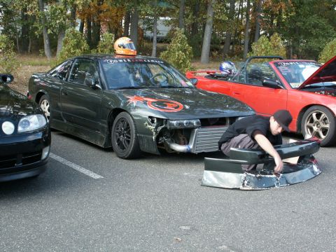 2001 Mercury Grand Marquis - A person works on the front bumper of a modified Nissan 240SX, with other cars parked nearby.