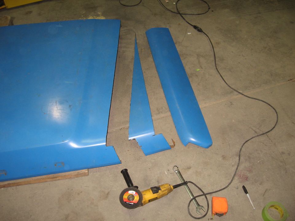Blue car hood and fender pieces with an angle grinder and wrench on a concrete floor