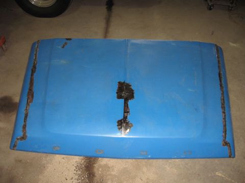 1977 Ford F-150 - A blue truck hood shows extensive rust damage along its edges and a large patch in the center.