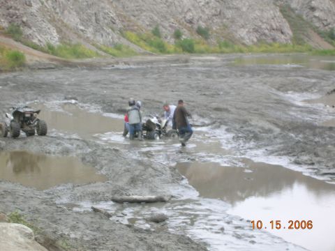 1985 Ford Bronco - Several ATVs are being ridden through a muddy, watery area with a rocky hillside in the background.