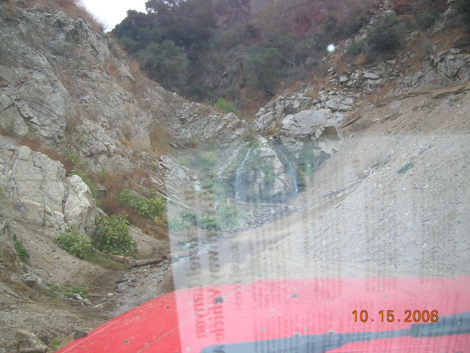Red vehicle hood in foreground, rocky hillside with waterfall, date stamp 10.15.2006
