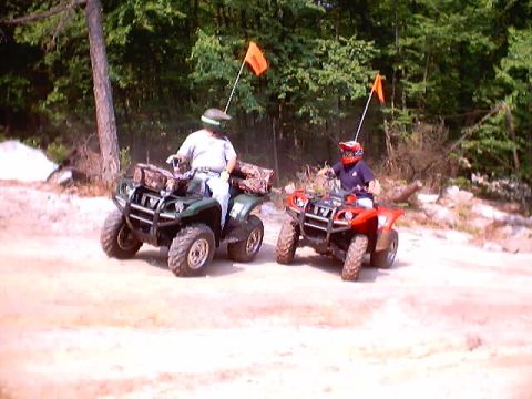 2001 Ford Escape - Two riders on ATVs navigate a dirt trail, each with an orange safety flag.