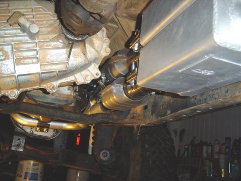 1986 Ford Bronco - Underside view of a vehicle showing an exhaust system with a polished stainless muffler and clamp connections, mounted alongside a metal fu…