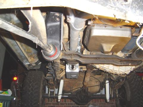 1986 Ford Bronco - Underside view of a vehicle showing the frame, exhaust piping, transmission crossmember, fuel tank, and rear axle with white shock absorber…