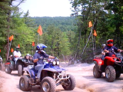 2001 Ford Escape - A group of ATVs are riding on a dusty trail surrounded by trees, with orange flags visible on some of them.