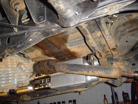 1986 Ford Bronco - Underside view of a vehicle on a lift, showing the driveshaft with U-joints, a stainless steel muffler/exhaust component, and surrounding c…